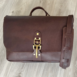 Teczka brązowa ze skóry listonoszka A4 na ramię z mosiężną klamrą.