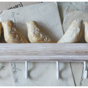 Wieszak z kremowymi ptaszkami na bielonym drewnie